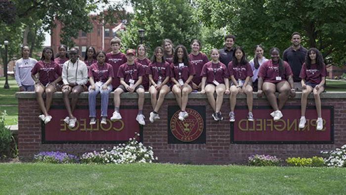 Students in the Social Justice and Health Professions Academy sit on the Springfield College sign on the Naismith Green